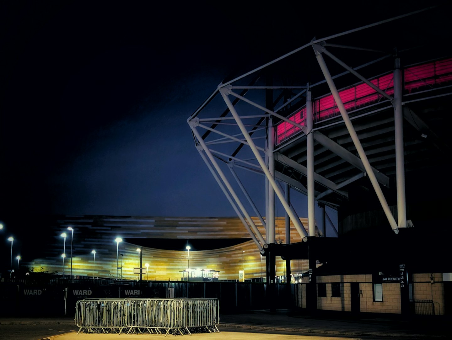 Modern stadium with pink lights and yellow panels at night.